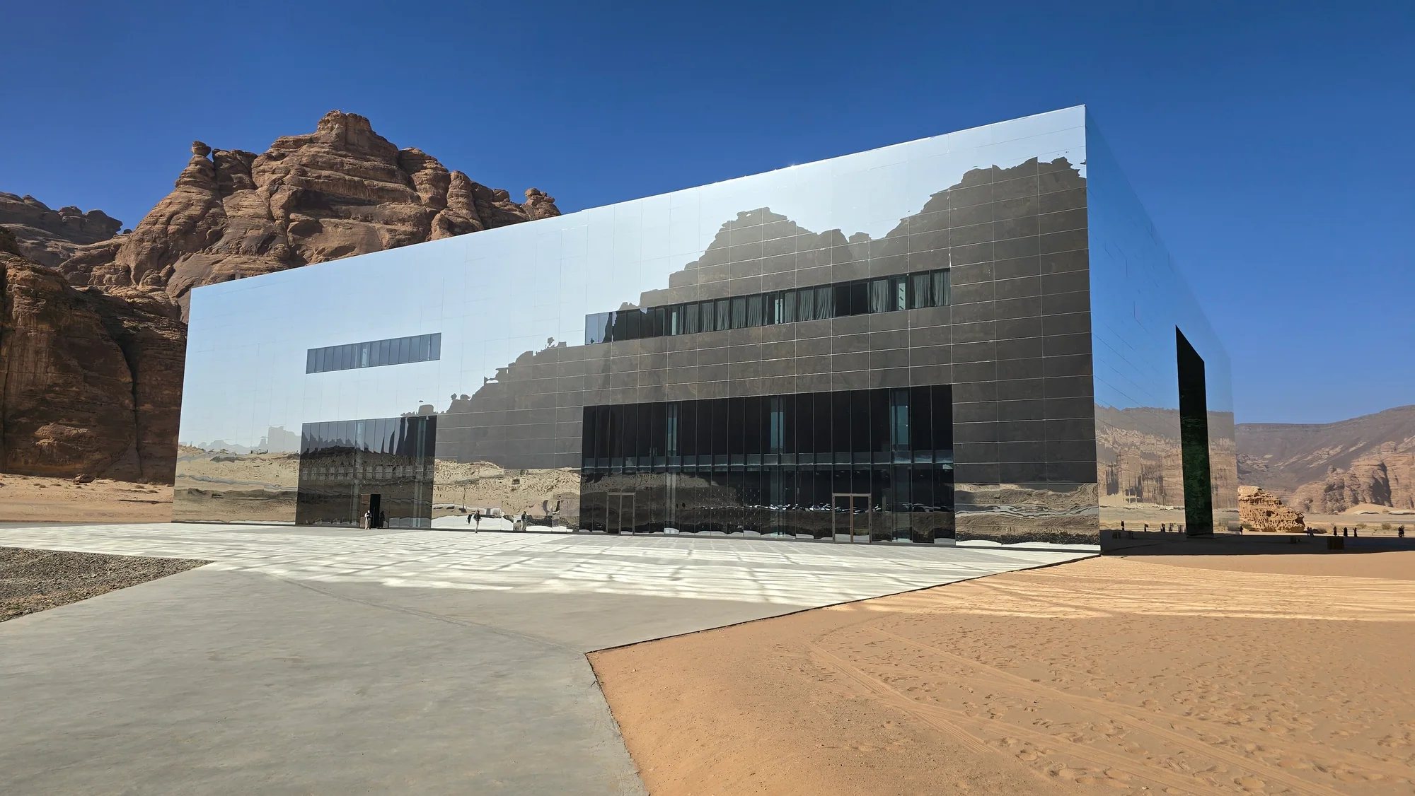 A mirrored rectangular pavilion reflecting sandstone cliffs in a desert basin.